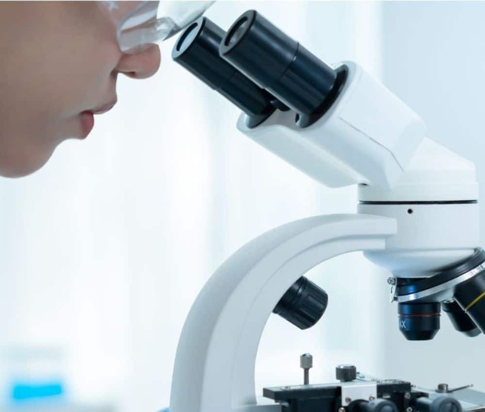 A vet wearing a lab coat uses a microscope